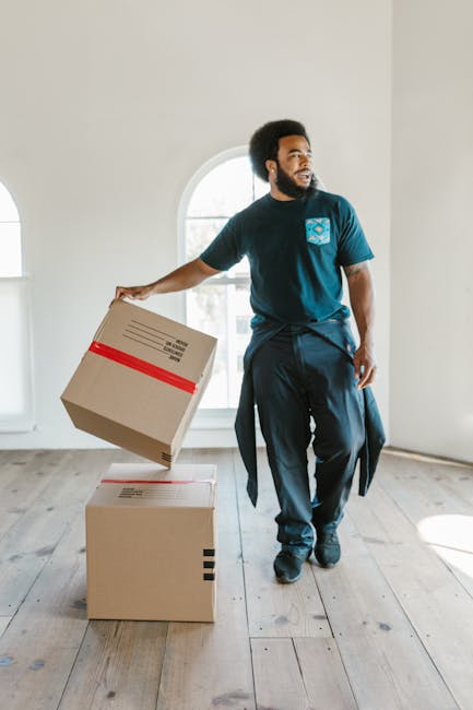 Two movers from Man and a Van Harringay are engaged in a home relocation process outside a building with a brick wall and decorative glass window. They are handling several cardboard boxes sealed with